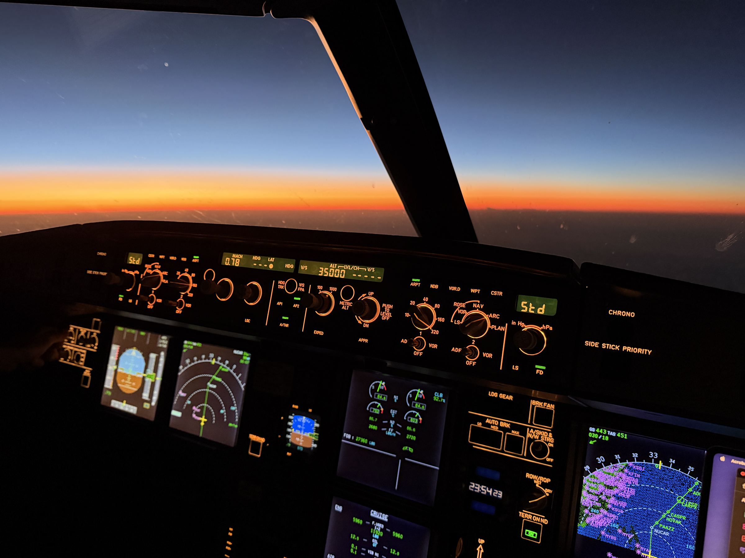 An airliner flight deck at dusk, panel lit, the horizon glowing through the windshield